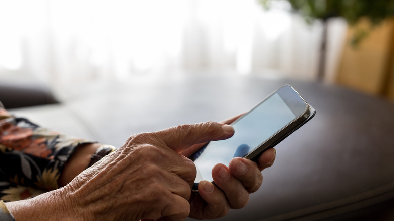 A close-up shot of an older person's hand using a finger to navigate a brightly lit smartphone screen.