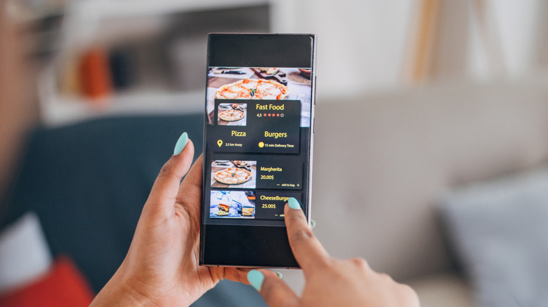 A woman holding a smartphone displaying food and restaurant search results.