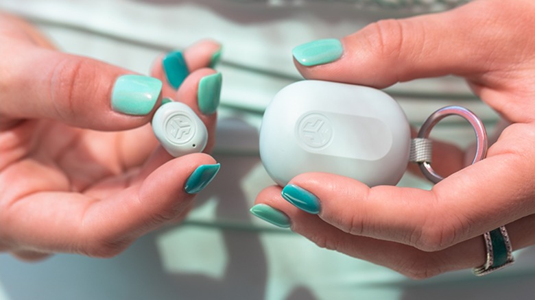 A person holding a mint-colored JBuds Mini case and a single tiny earbud.
