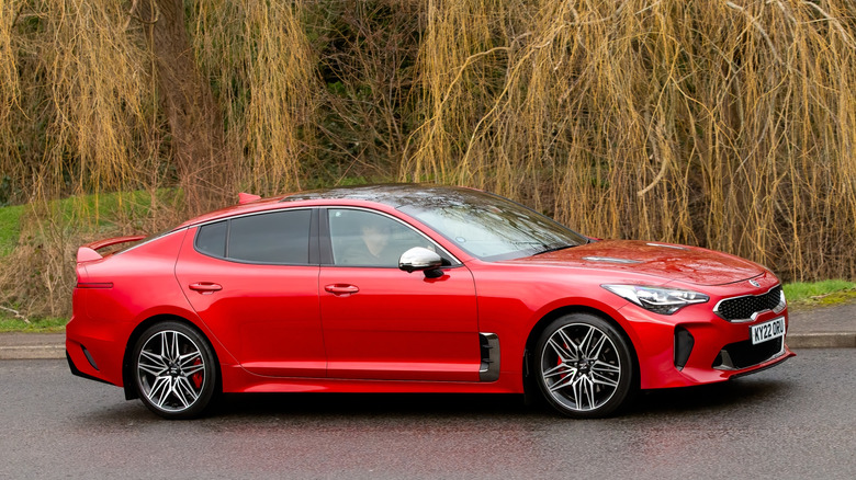 A red Kia Stinger GT driving on a winding country road.
