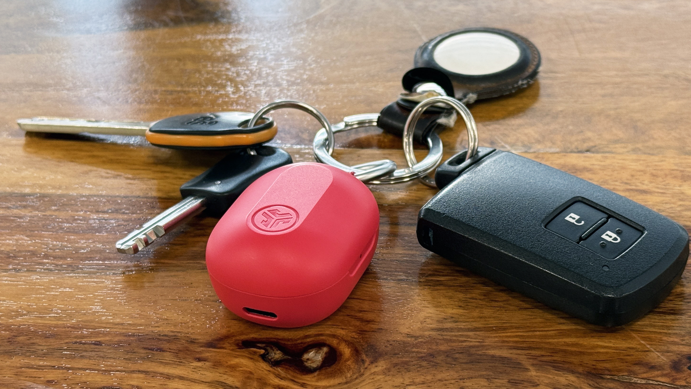 JLab JBuds Mini case placed next to a standard car key fob for size comparison.