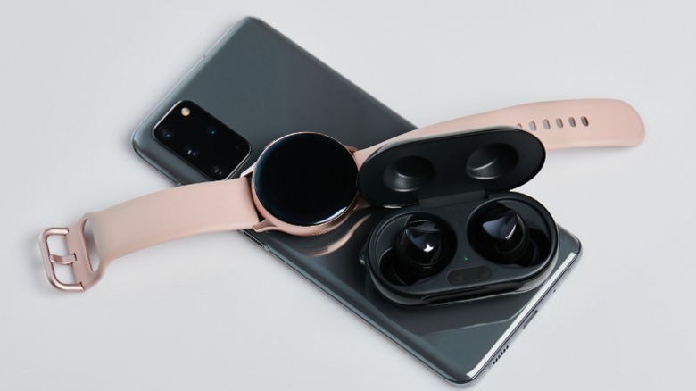 A smartphone wirelessly charging a smartwatch and earbuds placed on its back.