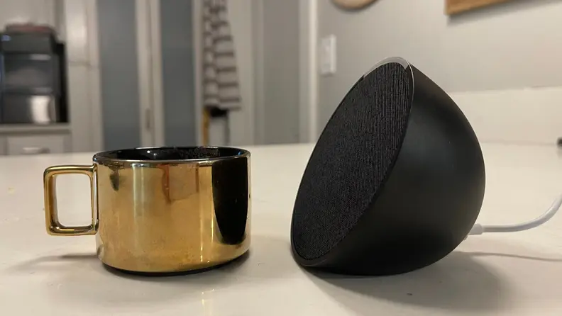 Amazon Echo Pop placed next to an espresso cup on a table.