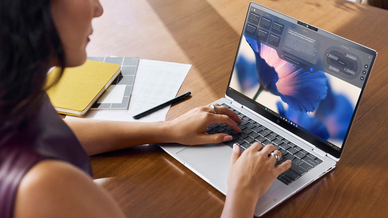 A person working on a thin laptop at a tidy wooden desk with minimal accessories.