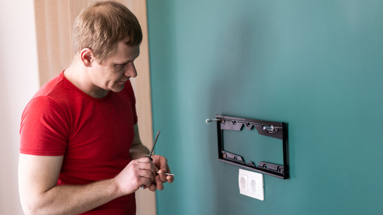 The installation process of a metal wall-mount bracket being leveled on a colored wall.