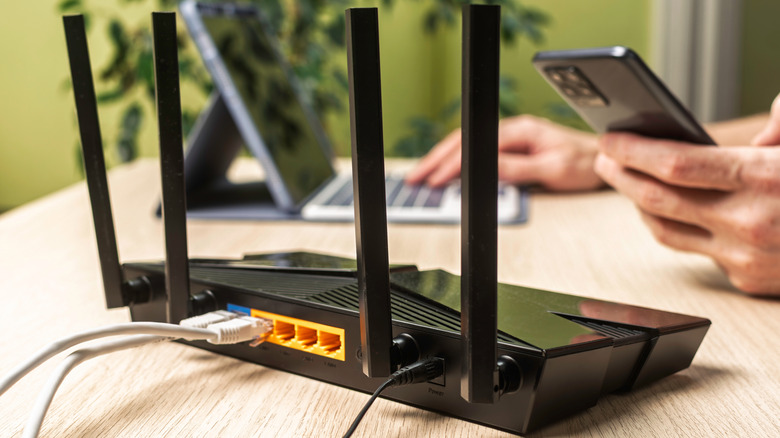 A black Wi-Fi router with four vertical antennas standing on a surface.