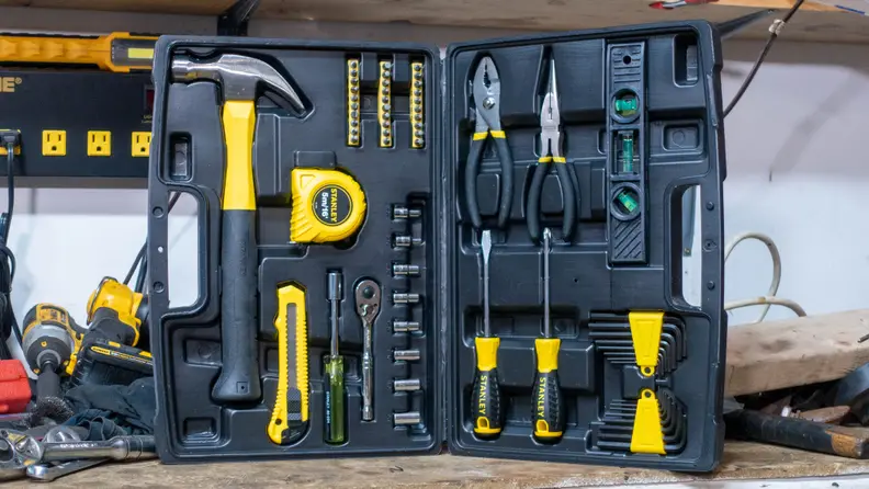An open Stanley 65-piece tool kit resting on a wooden workbench.