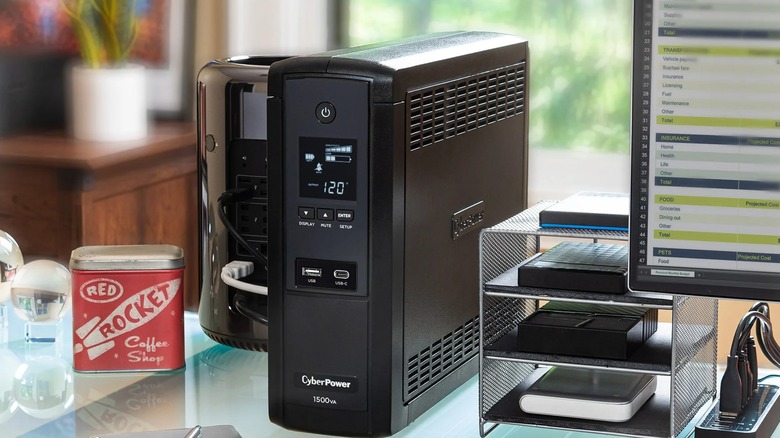 A CyberPower uninterruptible power supply unit placed on a desk next to a gaming PC.