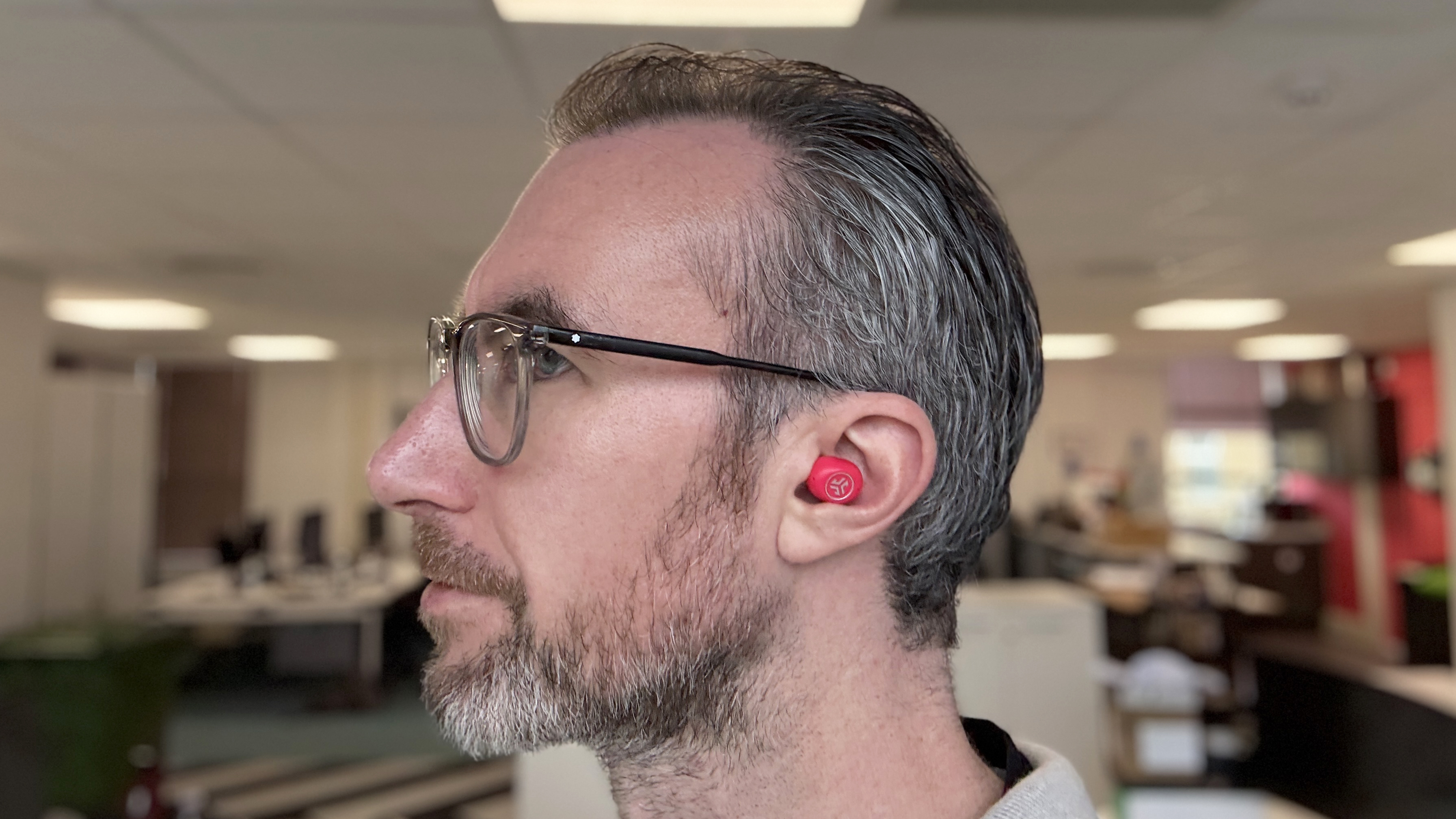 A man wearing the JLab JBuds Mini earbuds while working in an office.