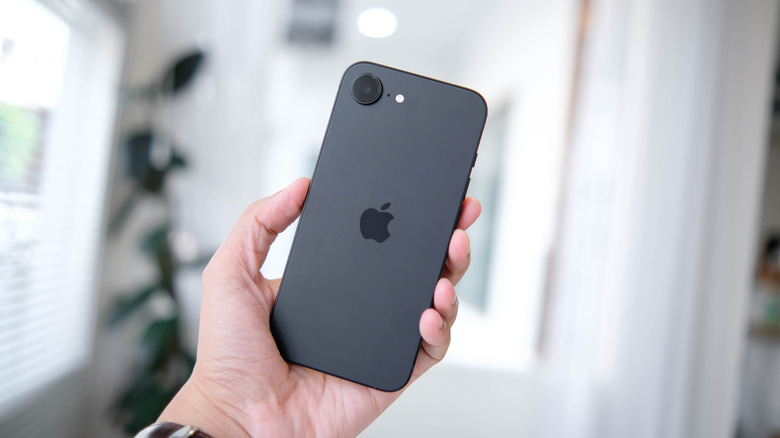 A hand holding a smartphone with a single-lens rear camera housing.
